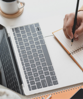 Person taking notes in front of a laptop.